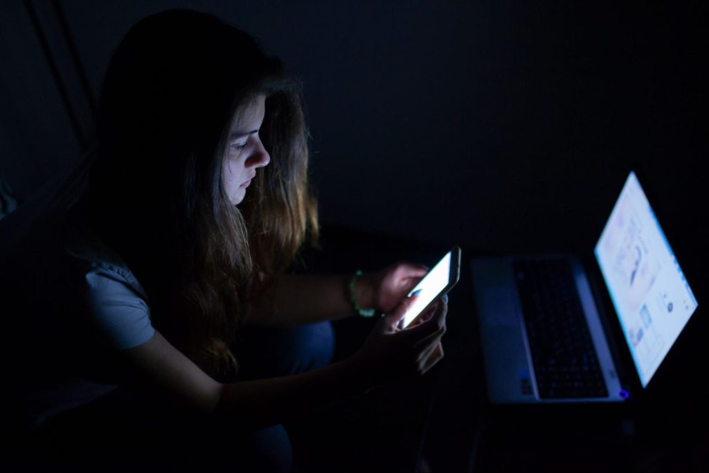 Teen on phone and laptop at night